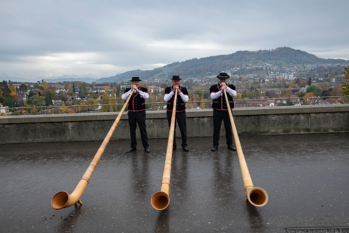 Bern, Switzerland - October 30, 2021: A Swiss alphorn trio plays on a rainy autumn day at the Bundeshausterrasse in Bern.