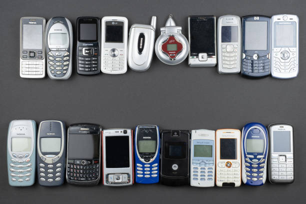 una gran cantidad de teléfonos móviles antiguos usados con teclados, varias marcas. muchos tipos y generaciones de dispositivos móviles para teléfonos inteligentes en fila. editorial - nokia fotografías e imágenes de stock