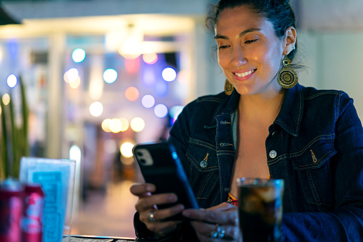 young latin woman looking at mobile device in a restaurant or pub portrait