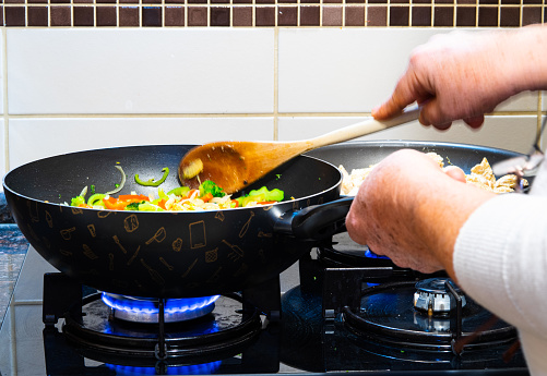 Blurry hands cooking vegetables in black pan at home