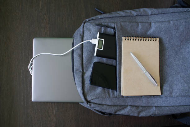 Modern laptop backpack lies with an external battery, smartphone, notepad, pen and silver laptop on a wooden table. The concept of using and recharging gadgets while studying and traveling Modern laptop backpack lies with an external battery, smartphone, notepad, pen and silver laptop on a wooden table. The concept of using and recharging gadgets while studying and traveling. Close-up wooden flash drive stock pictures, royalty-free photos & images