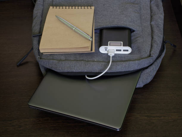 istock Modern laptop backpack sits on a wooden table along with a silver laptop, power bank, notepad and pen. The concept of recharging gadgets while studying, traveling and trip 1365650983