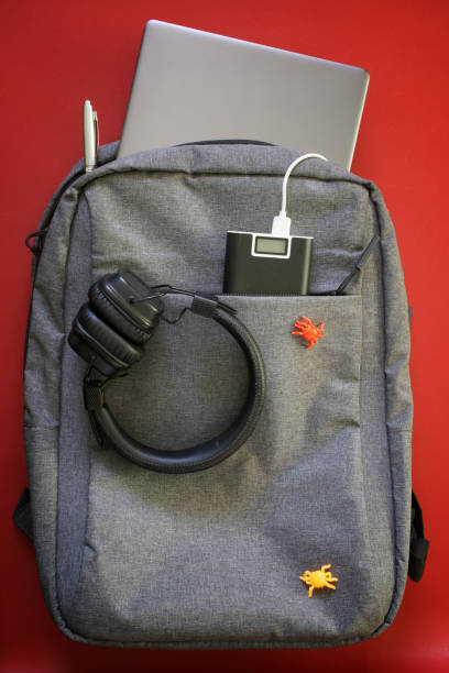 istock Modern laptop backpack with gadgets: headphones, smartphone, laptop and external battery. Red background. The concept of recharging gadgets while studying, traveling and trip 1365651008