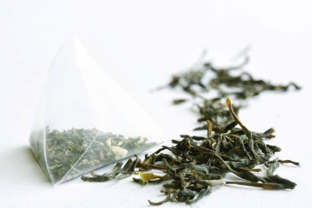 istock Tea bag pyramid with green tea on a white surface. Macro. Selective focusing. Daylight 1365651015