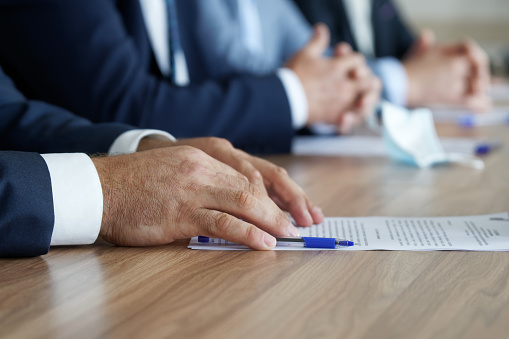 A man in an elegant suit holds his hands on the table, next to a document, during a work meeting. Without a face. Boss, deputy, politician, official, lawyer or businessman. Close-up