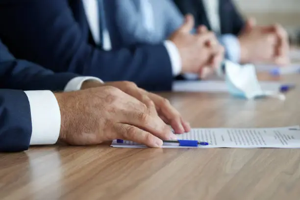 Photo of A man in an elegant suit holds his hands on the table, next to a document, during a work meeting. Without a face. Boss, deputy, politician, official, lawyer or businessman