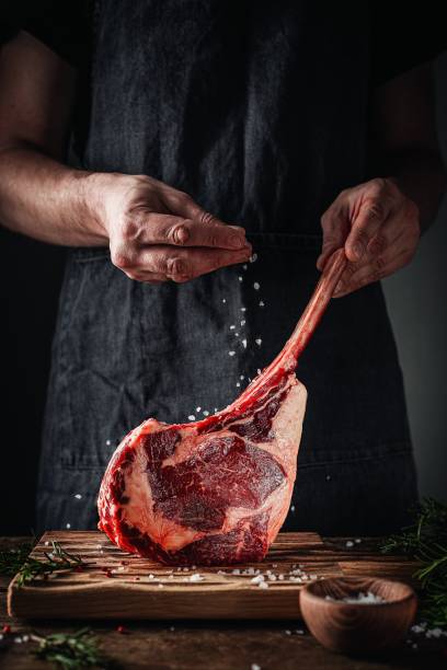 tomahawk steak in man’s hands Fresh meat with salt and rosemary rib eye steak stock pictures, royalty-free photos & images