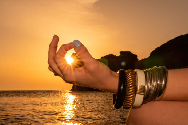 istock Young woman with long hair in white swimsuit and boho style braclets practicing outdoors on yoga mat by the sea on a sunset. Women's yoga fitness routine. Healthy lifestyle, harmony and meditation 1365657602