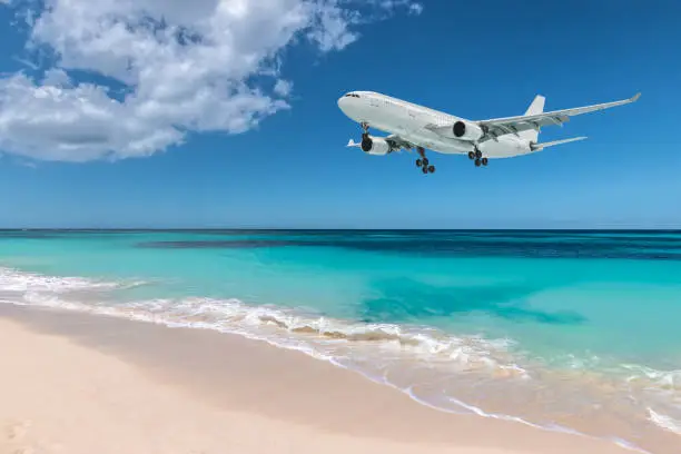 White airplane flying over turquoise colored sea and white sand beach, Maho Bay, Sint Maarten, Caribbean, Lesser Antilles. Travel and transportation concept.