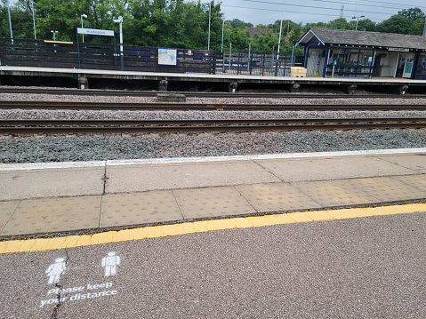 The station platform at Huntingdon, Cambridgeshire, England, UK, during the Covid-19 pandemic.  In the foreground is a sign asking passengers to keep their distance.