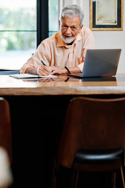 istock A happy senior student is sitting at home and writing down notes in a notebook while following an online lecture on the laptop. 1365665011