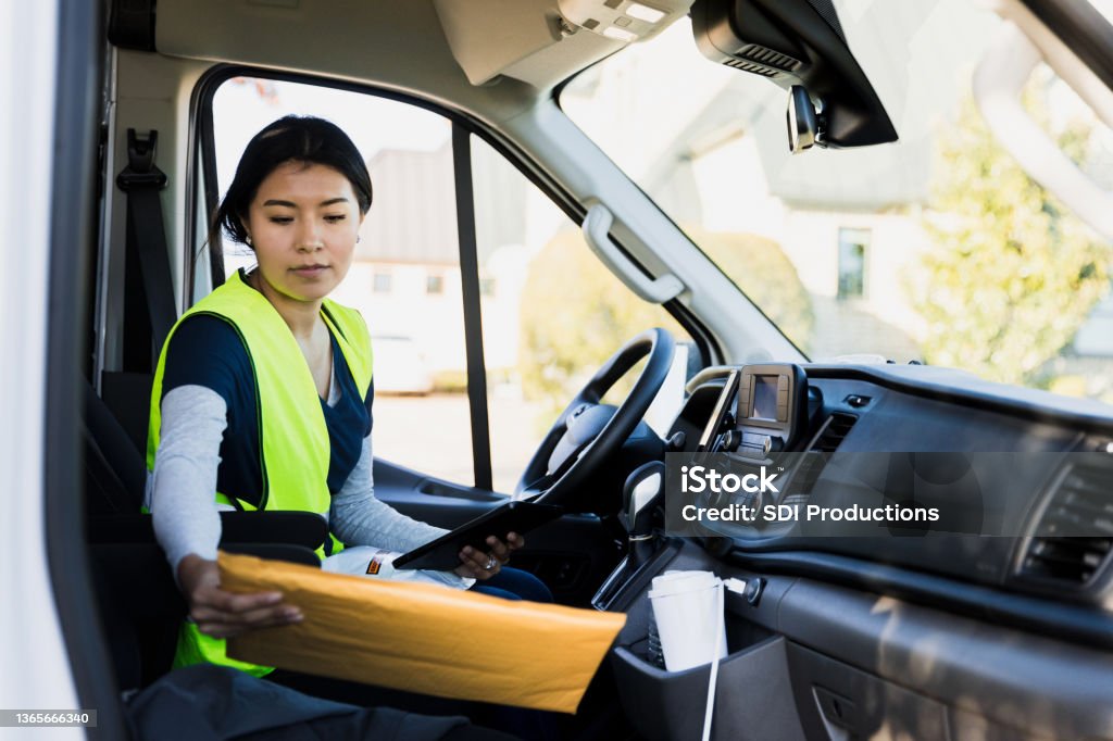 Delivery driver reads address on package Before delivering a package, a female delivery person ensures she is at the correct address. She is reading the address on the package. Delivery Person Stock Photo