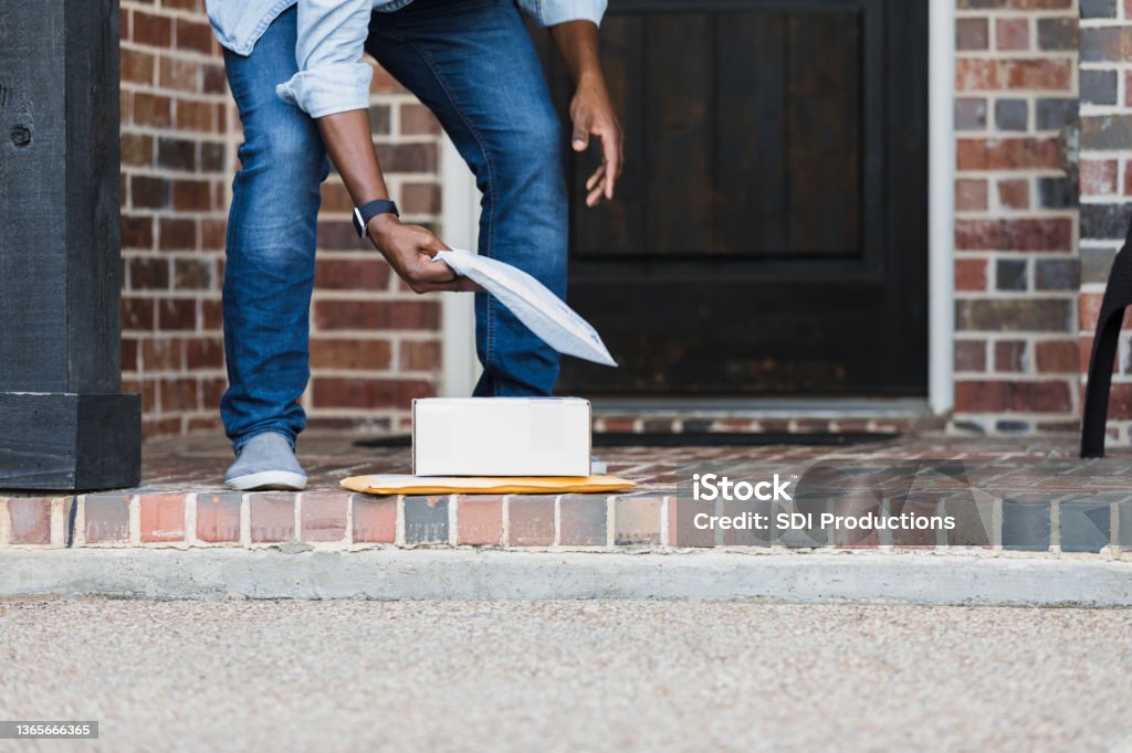 Unrecognizable man picks up packages on doorstep An unrecognizable man bends over to pick up packages that were left on his front porch by a delivery driver. Package Stock Photo