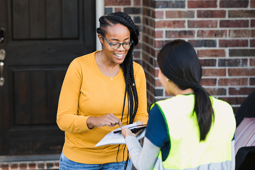 The smiling mid adult woman signs for her package on the digital tablet held by the unrecognizable female delivery person.