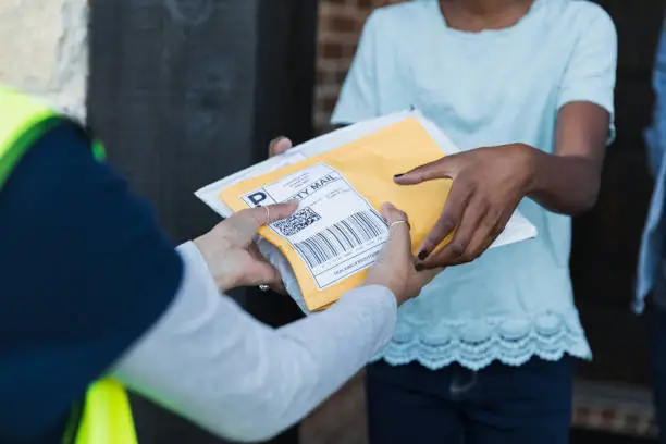 The focus of the photo is on the hands of an unrecognizable young girl as she receives packages from the hands of an unrecognizable female delivery person.