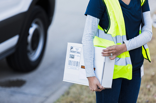 An unrecognizable delivery woman carries a package with the barcode and the QR code on its label.