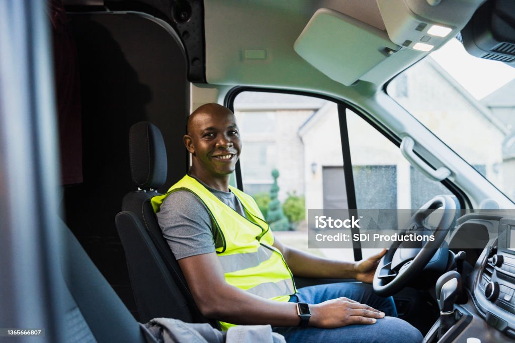 Mid adult male gig employee smiles from driver's seat The mid adult gig worker smiles from the driver's seat of his delivery van. Driving Stock Photo