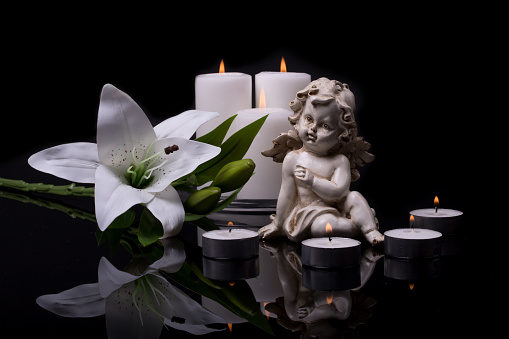 Ángel blanco con velas y flor de lirio blanco sobre un fondo negro photo