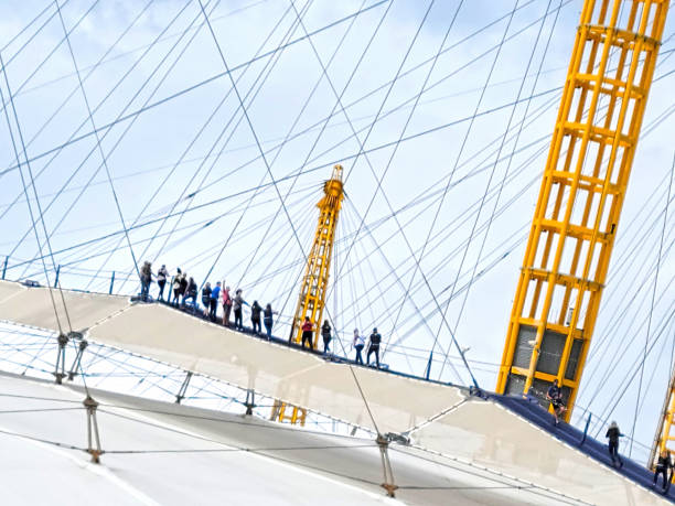 The O2 arena in London, England, UK, with a group of tourists walking over the top of the dome on a bright summer day in 2021.