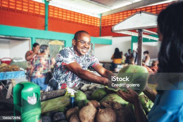 Smiling Young Market Vendor Giving Fresh Coconut To Female Client Stock Photo - Download Image Now