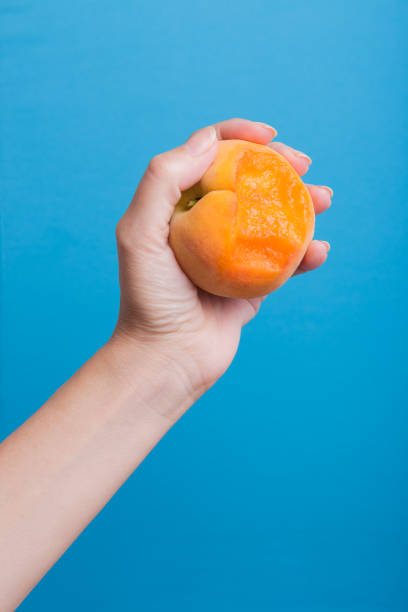 Woman's hand holding bitten peach blue background, healthy food concept