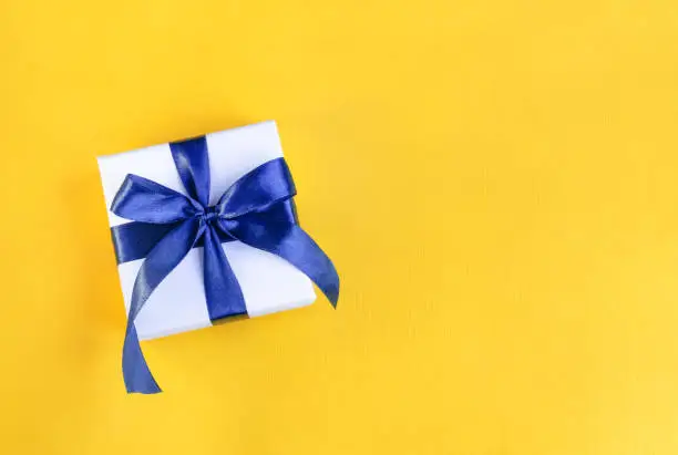 Photo of Banner of a Gift wrapped in white paper with a blue bow made of satin on festive yellow orange background