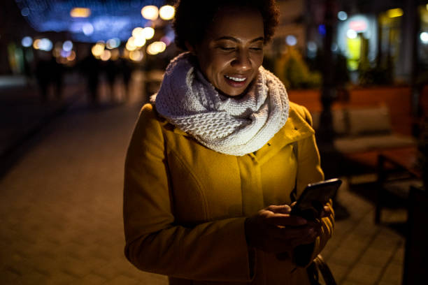 istock Smiling Young African American woman Text Messaging at night time 1365677409