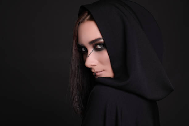 istock Mysterious witch in mantle with hood on black background 1365677676