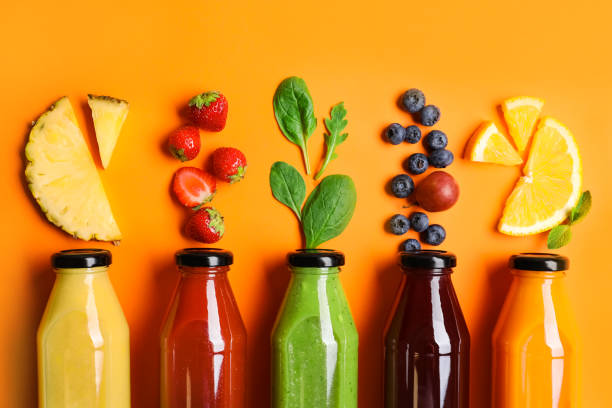 composición plana con botellas de deliciosos zumos e ingredientes frescos sobre fondo de naranja - freshly squeezed fotografías e imágenes de stock