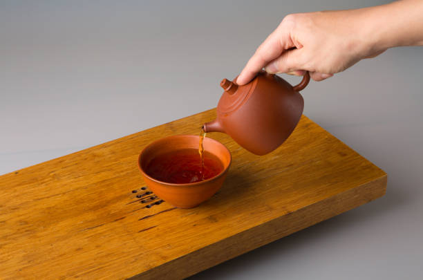 istock A man's hand pours freshly brewed pu erh tea from a clay teapot into a traditional cup. A cup on a table for tea ceremonies 1365680576