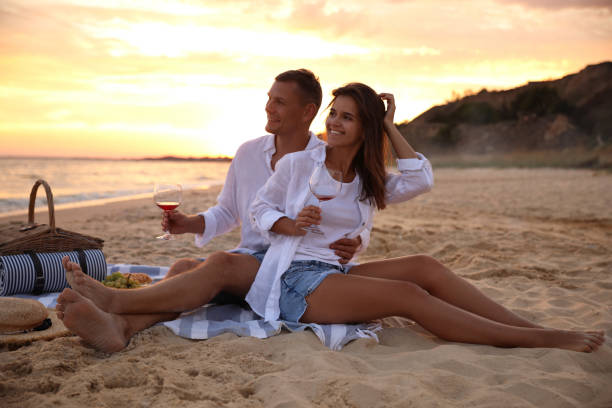istock Lovely couple having romantic picnic on beach at sunset 1365682141