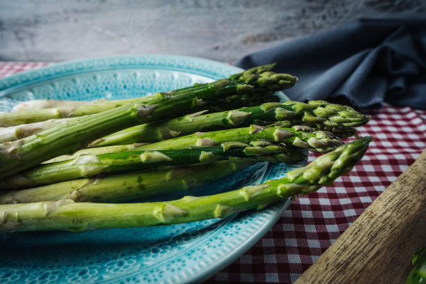 Group of raw green asparagus on a vintage plate on a table with a checkered tablecloth. High view Group of raw green asparagus on a vintage plate on a table with a checkered tablecloth. eating asparagus stock pictures, royalty-free photos & images