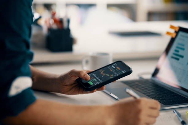 Mid adult man checking financial information on a smart phone while doing his bookkeeping Mid adult man checking financial information on a smart phone while doing his bookkeeping in his home office in Japan.  Depicts TradingView financial market chart. making money stock pictures, royalty-free photos & images