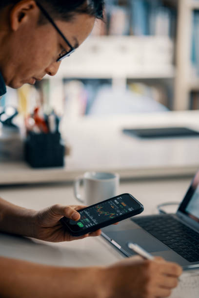 istock Mid adult man checking financial information on a smart phone while doing his bookkeeping 1365692267