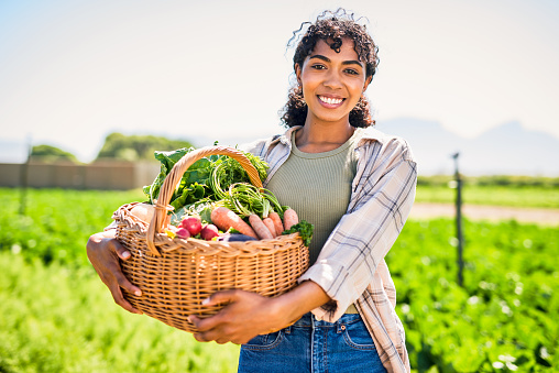 Portrait of a young woman carrying a crate of fresh produce on a farm