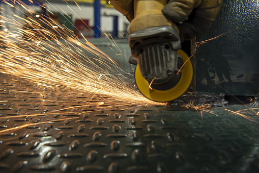 Sparks flying as worker smooths out rough welds on steel, using an angle grinder with an abrasive wheel (zirconia flap disk). Photo taken in Gainesville, Florida. Nikon D750 with Nikon 24-70 ED VR lens
