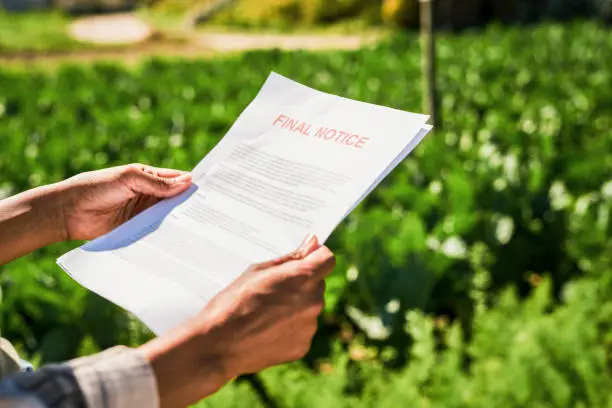 Photo of Closeup shot of an unrecognisable woman holding a letter of final notice on a farm