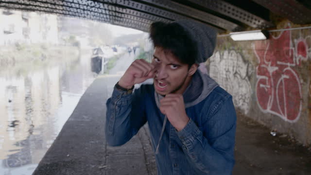 Portrait tough, aggressive young man punching at camera under urban canal bridge