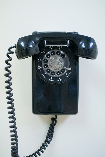 Black and dusty old rotary phone hangs on a white wall