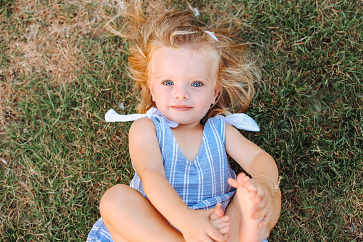 Directly above view portrait of a cute blonde preschooler child lying on the grass