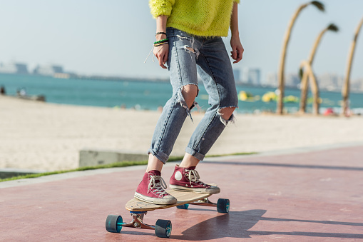 Hipster girl long-boarding near the beach on a summer day. Cropped closeup of legs.