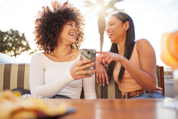 Shot of two friends sharing a funny moment while using a cellphone and having drinks Please send that to me! mobile phone text messaging telephone women stock pictures, royalty-free photos & images