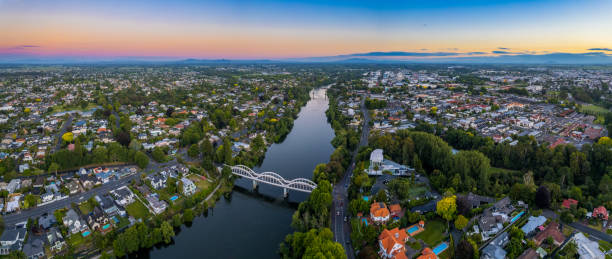 Aerial panoramic drone view at sunset of Hamilton City (Kirikiriroa) in the Waikato Region of New Zealand, Aotearoa A drone captured view looking towards the central business district (CBD) from the Fairfield Bridge over the Waikato River as it cuts through the city of Hamilton, in Waikato, New Zealand. waikato river stock pictures, royalty-free photos & images