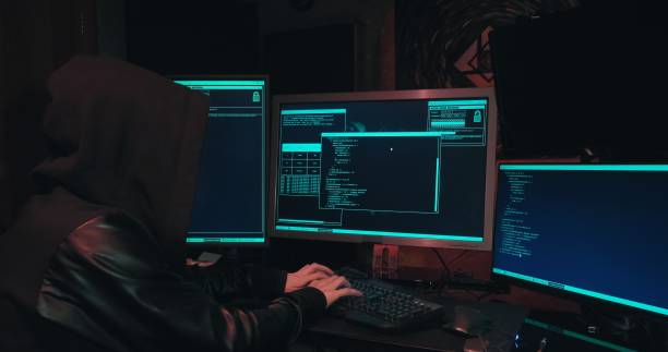 istock Hacker in a hood sits in front of computer screens and hacks databases 1365709608