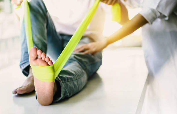 看護師は、患者が脚の筋力低下の治療のための柔軟性の練習でストレッチ演習を行うのを助けます。 - バイオメカニクス ストックフォトと画像