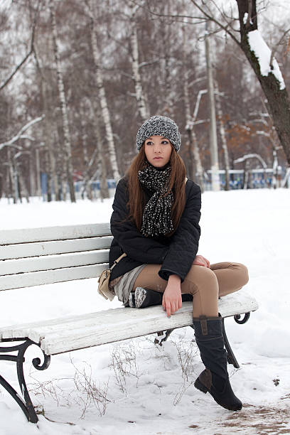 Girl sits on a bench in the park in the winter