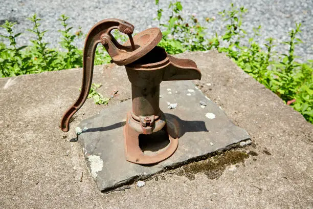 Photo of Rusty Manual Water Pump on Stone Well Cap with Moss