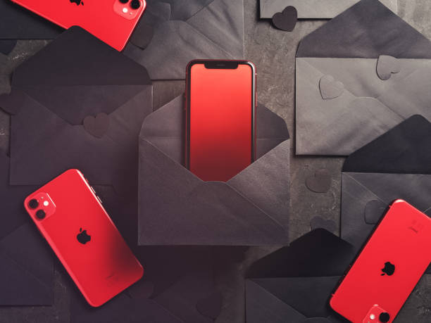 Red iPhones 11 is on a dark background with black envelopes and paper figures in the form of hearts. Minimal composition. Flat lay. Copy space. stock photo