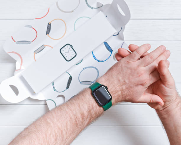 new apple watch series 7 in green is worn on a man's hand over branded paper packaging against the background of a white wooden table. stock photo