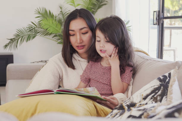 azjatycka matka czytała książkę swojej mieszanej córce w domu, spędzając razem czas z rodziną, koncepcja edukacji domowej - mother superior zdjęcia i obrazy z banku zdjęć